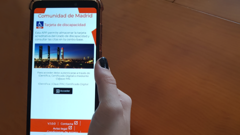 Imagen de una mano que sujeta un móvil con la App "Tarjeta de discapacidad" y logotipo de la aplicación