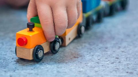Detalle de la mano de un bebé que juega con un tren de madera