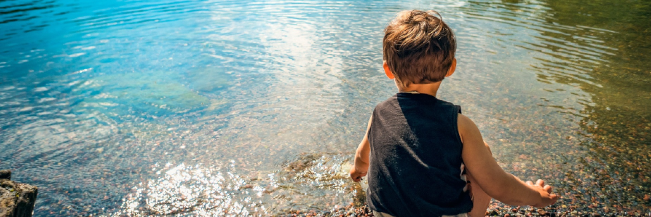 niño agachado en la orilla de un lago