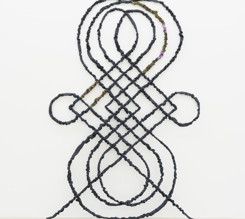 Escultura de acero y textil que tiene forma de reja con motivos curvos vegetales