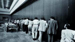 Marisa Flórez. Periodistas concentrados en busca de información durante una reunión a puerta cerrada del Consejo político de la UCD. Madrid, 1982. © Marisa Flórez, 2026 Varios hombres escuchando a través de una pared