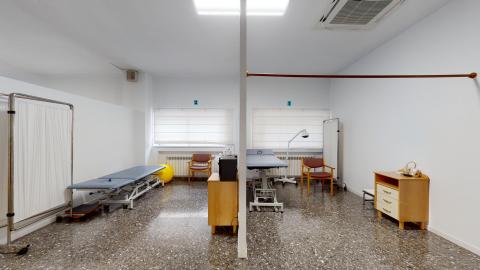 Dos espacios diferenciados con camillas de fisioterapia. Al fondo ventanas con cortinas blancas traslúcidas. 