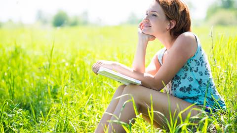 chica feliz leyendo sentada en la hierba