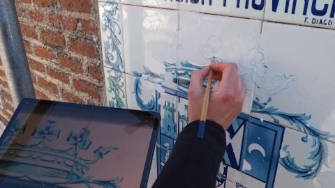 Azulejos sobre fachada de ladrillo en mal estado, una mano en primer plano sosteniendo un pincel