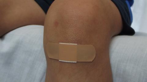 Rodilla de niño pequeño con herida cubierta por tirita