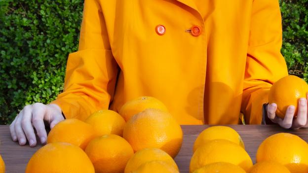 Mujer con chaqueta naranja y muchas naranjas en su regazo