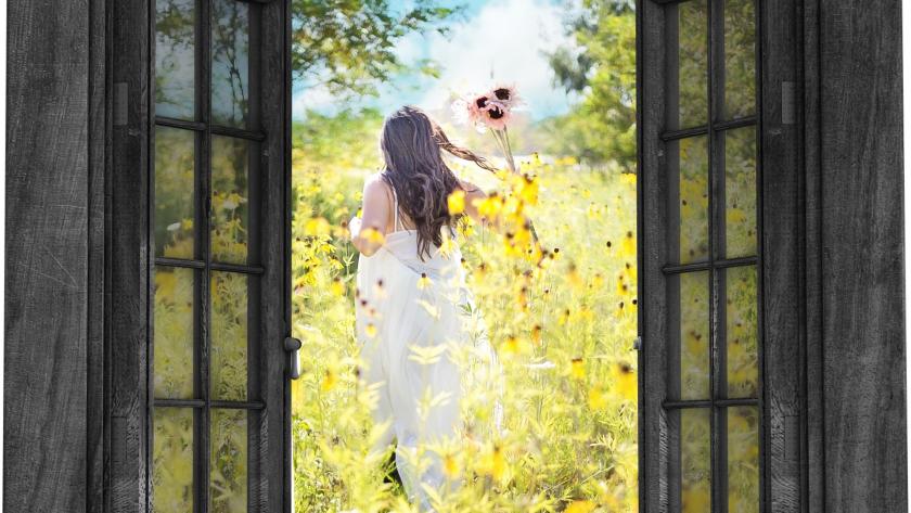 Ventana de una casa abierta a través de la que se ven flores y una mujer