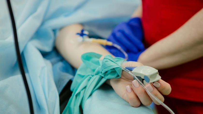 Paciente en una cama con un pulsioxímetro en el dedo, atendido por un profesional sanitario 