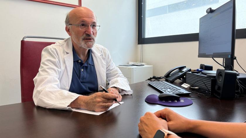 Doctor de frente atendiendo en consulta a paciente al que se le ven los brazos apoyados en mesa