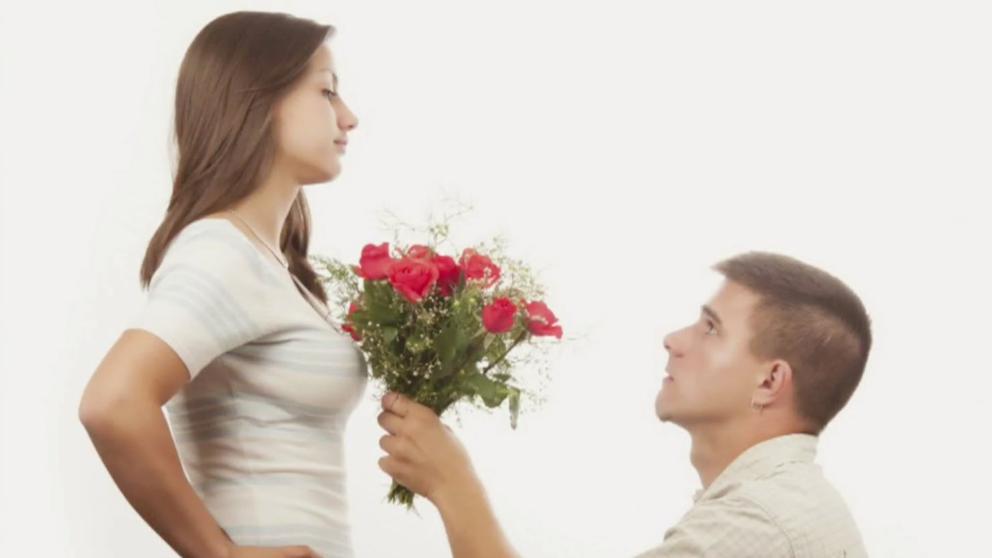 Hombre de rodillas entregando ramo de flores a mujer