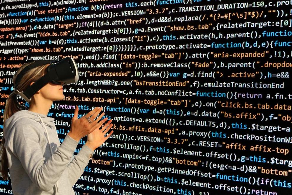 Persona utilizando gafas de realidad virtual y guantes tecnológicos frente a una pantalla con código informático.