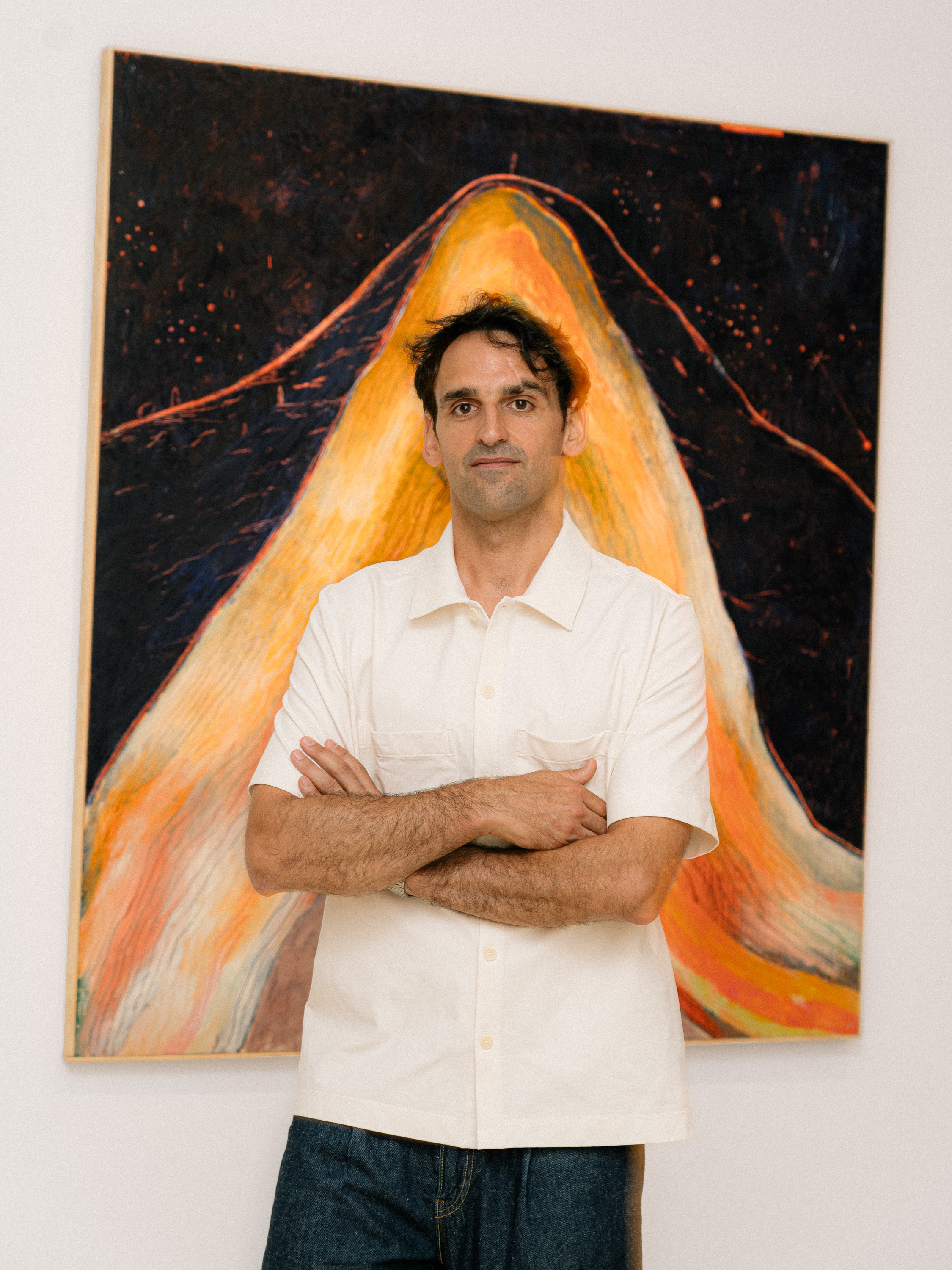 Retrato de Diego Delas. Fotografía: Maru Serrano Retrato de un hombre con camisa blanca frente a un lienzo que reprenta un volcán