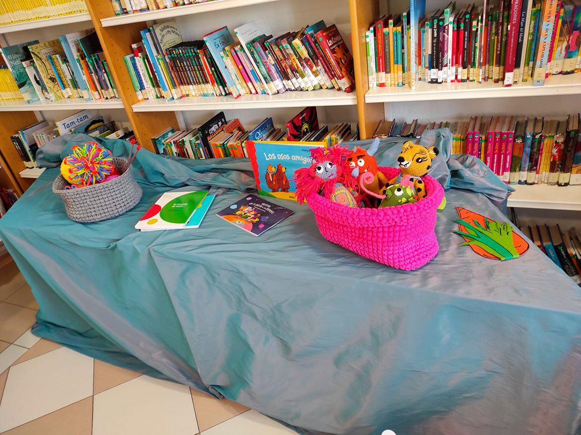 Mesa con muñecos y libros con estantería con libros al fondo