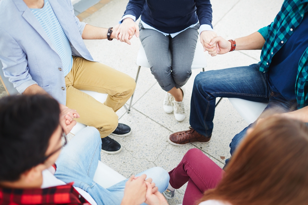 grupo de personas sentadas en círculo dándose la mano