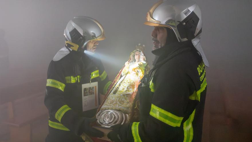dos bomberos evacuan la talla de una virgen en una estancia llena de humo
