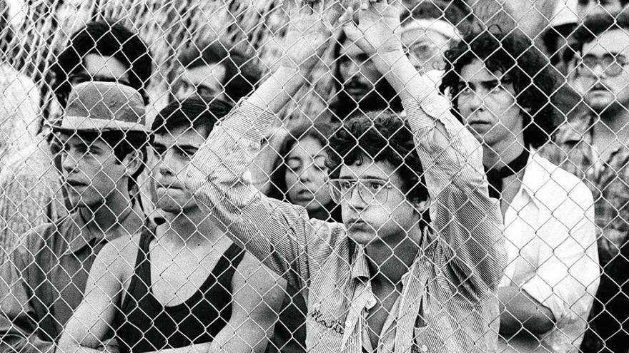 Varios jóvenes miran algo a través de una valla metélica