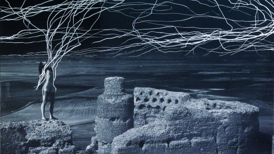 Mujer sobre unas ruinas y de la que se desprenden rayas que suben hacia el cielo