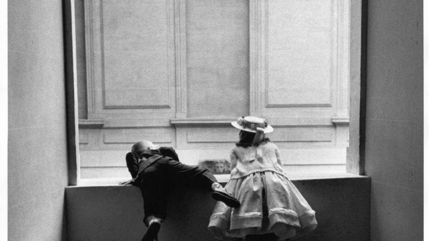 Niño y niña de espaldas asomados a una ventana