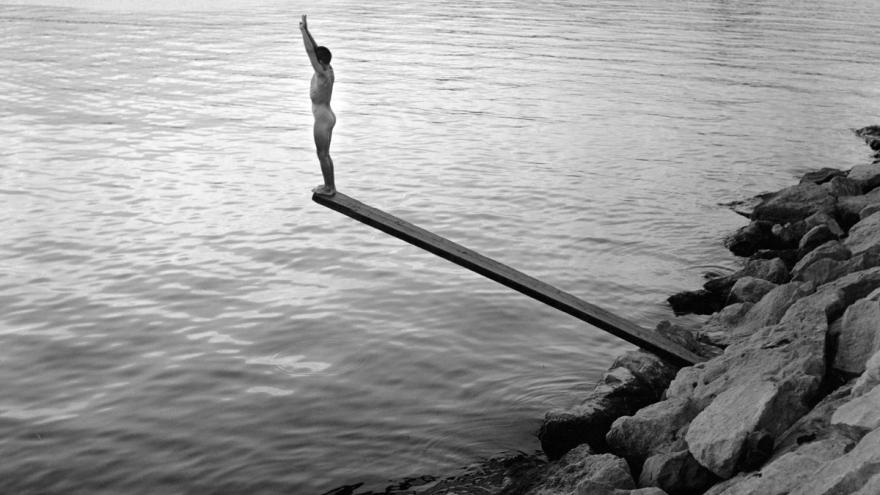 Joven en lo alto de un trampolín preparándose para saltar al mar