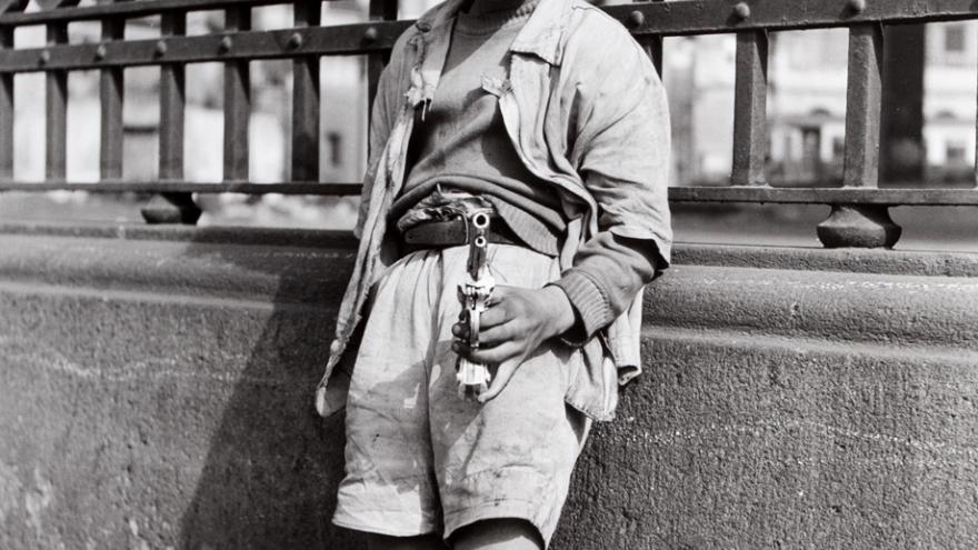 Niño con pistola de juguete posando delante de una verja
