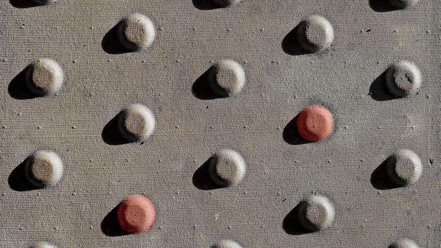 Detalle de tejido grisaceo con trama de resaltes redondos, dos de ellos rojizos