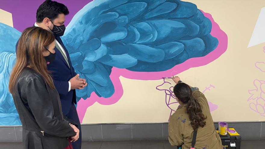 El consejero observa como la artista pinta el mural