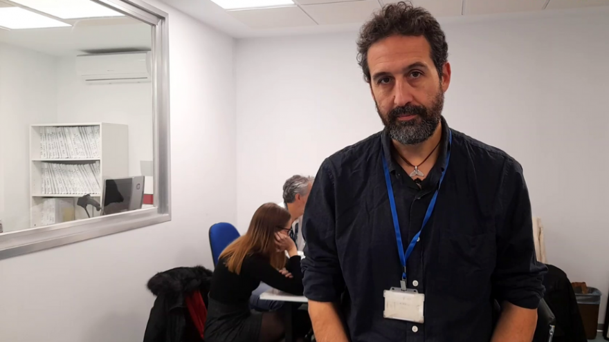 Hombre con barba posando delante de mesa con personas trabajando