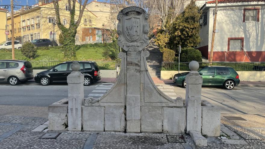 Imagen frontal fuente de piedra con dos columnas laterales, pilar central con escudo e inscripciones