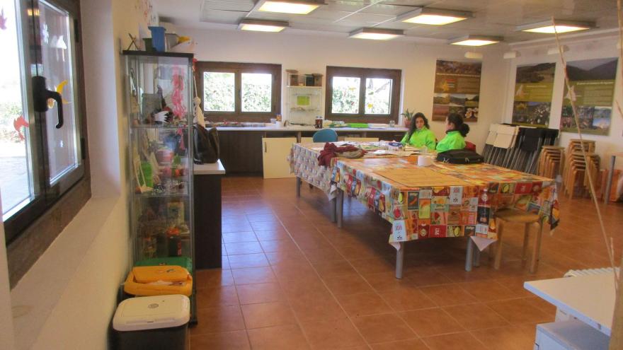 Habitación con mesa en el centro con dos monitoras sentadas, vitrina y poster en paredes
