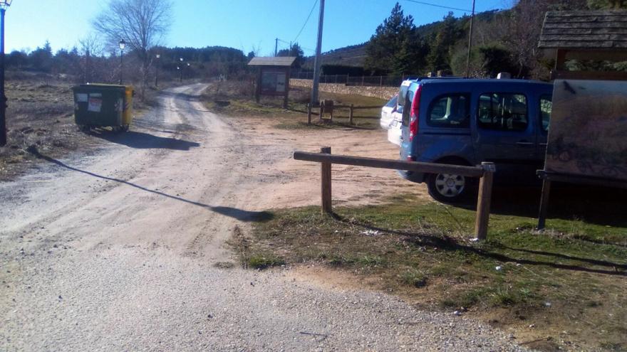 Zona de tierra señalizada con coches aparcados a la derecha y pista al fondo