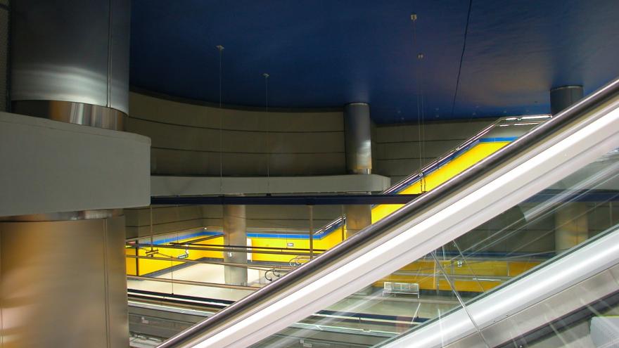 Estación Hospital de Móstoles, Vista desde las escaleras mecánicas, techo azul intenso, vitrex de la estación amarillo y columnas de acero