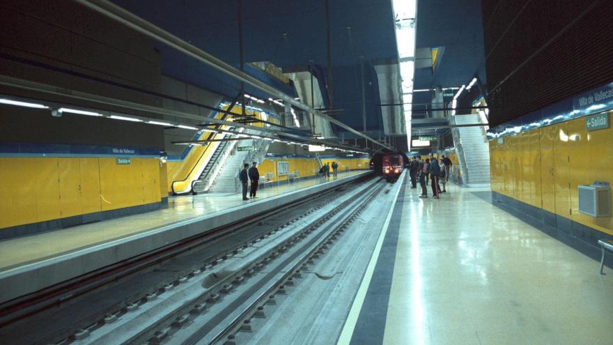 Tren entrando en la estación Villa de Vallecas, personas esperando en los andenes