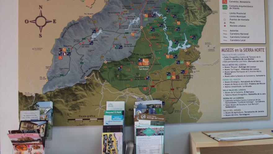 Mesas con folletos informativos y plano de la sierra norte con actividades en la pared