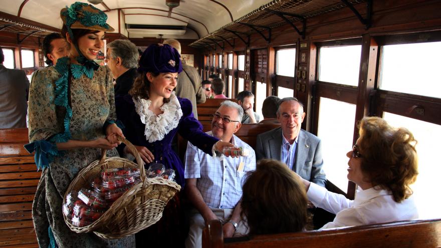 Pasajeros del Tren de la Fresa reciben una caja de fresas de dos mujeres vestidas de época