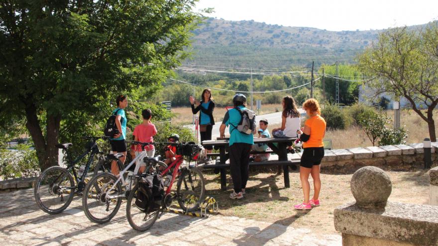 Zona de descanso con mesa de picnic, familia alrededor y bicis aparcadas.