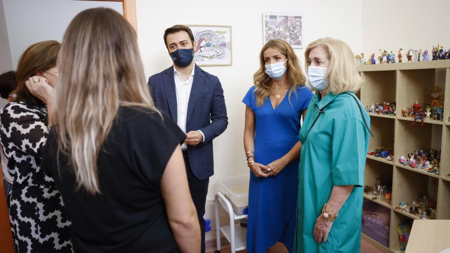 La consejera junto con otras mujeres y el Director General de Juventud hablando de pie en una sala con una estantería de fondo con figuiritas 
