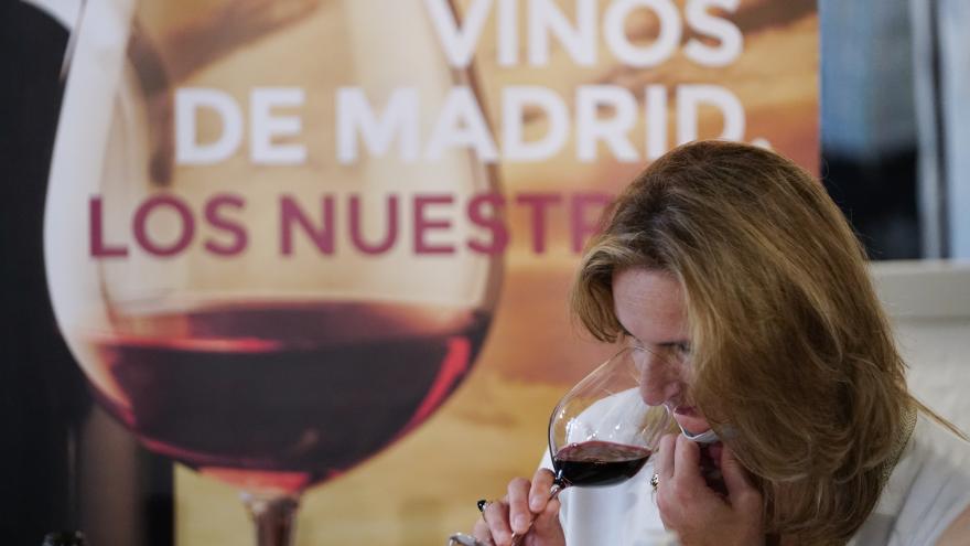 La consejera oliendo una copa de vino con el cartel oficial Vinos de Madrid de fondo