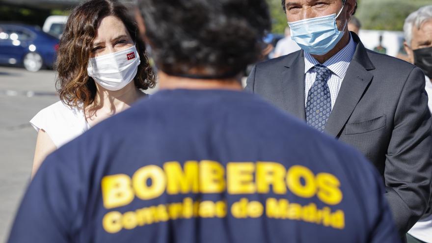 La presidenta de fondo y en primer plano un bombero de espaldas con una camiseta donde pone bomberos Comunidad de Madrid