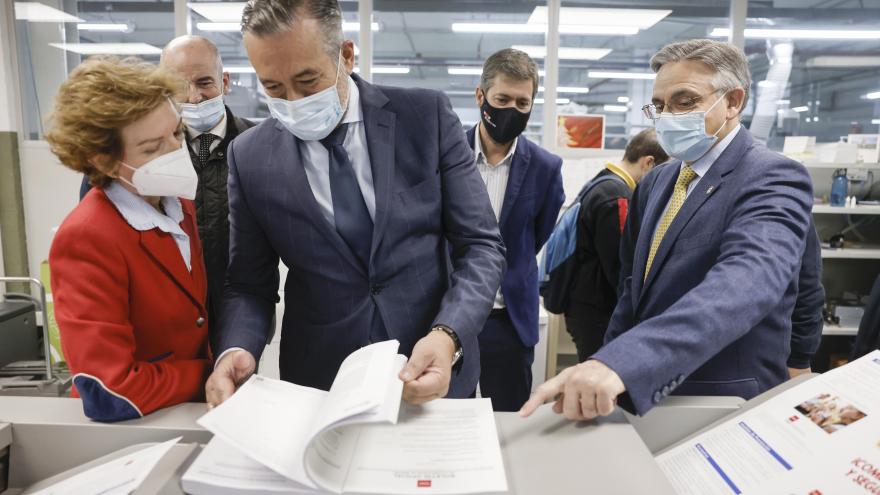 El consejero acompañado de trabajadores ojeando un libro