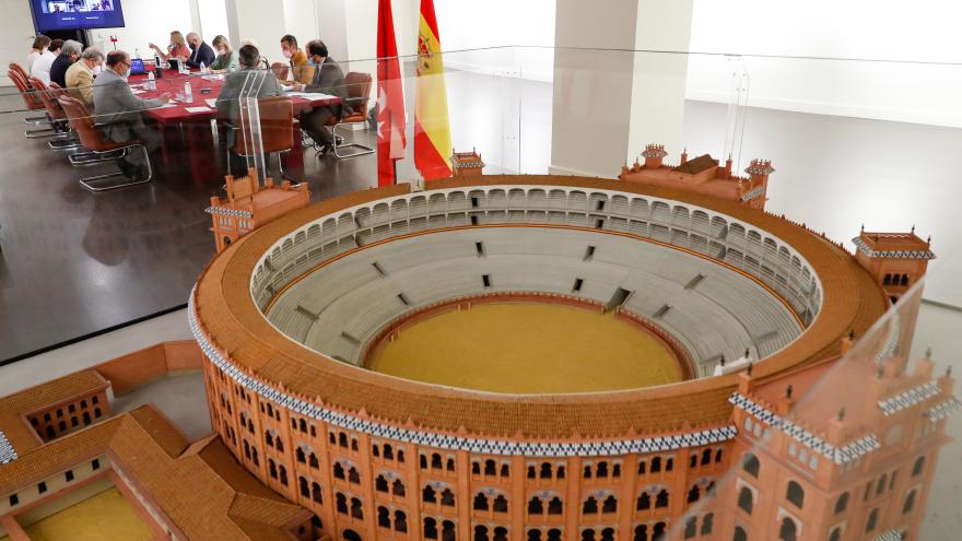 Primer plano de la maqueta de la Plaza de las Ventas y de fondo la mesa de la reunión con todos los participantes sentados