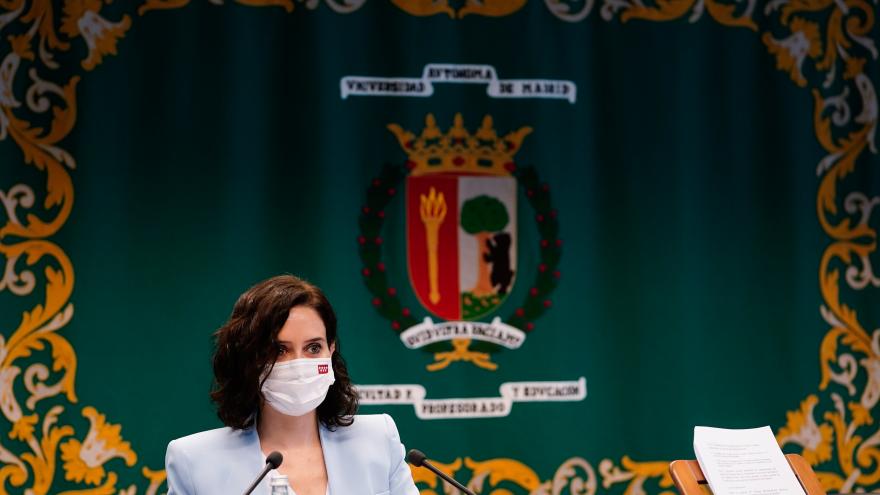 Isabel Díaz Ayuso sentada en la mesa delante de los micrófonos y de fondo el escudo de la universidad.