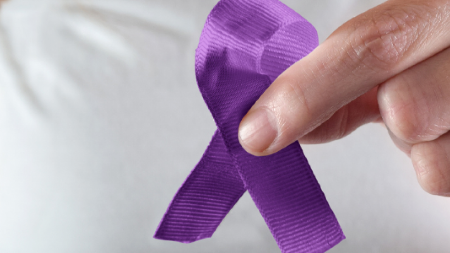 Mano que sujeta con dos dedos lazo morado