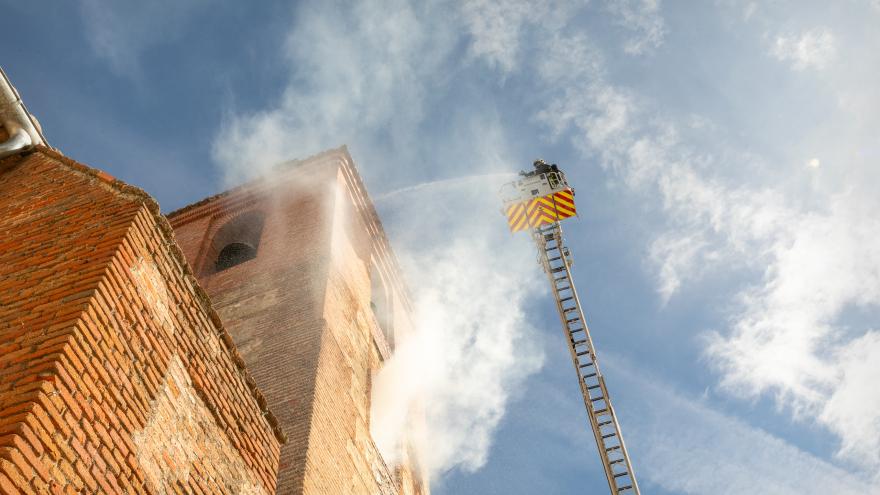 Un bombero en una escala extingue el humo que sale del torreón de una iglesia