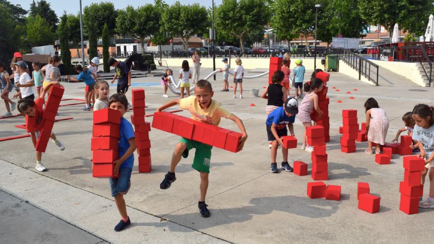 Niños y niñas jugando en una plaza con grandes cubos de color rojo