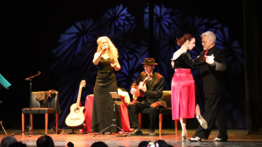 fotografía de escena muestra una mujer cantando, un hombre tocando la guitarra y un apareja bailando