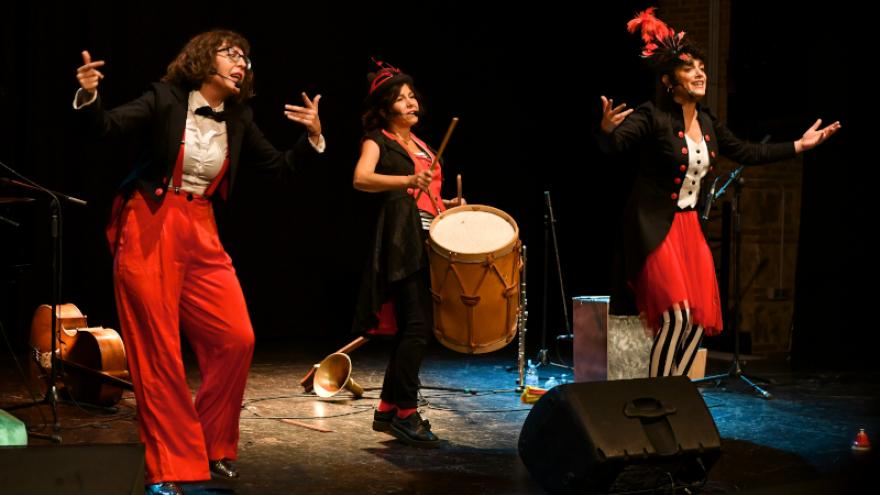 Fotografía de la compañía en escena, disfrazada de maestras de ceremonia tocando y cantando 