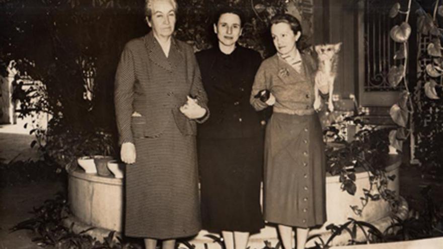 3 mujeres posando, una de ella con un perrito en brazos