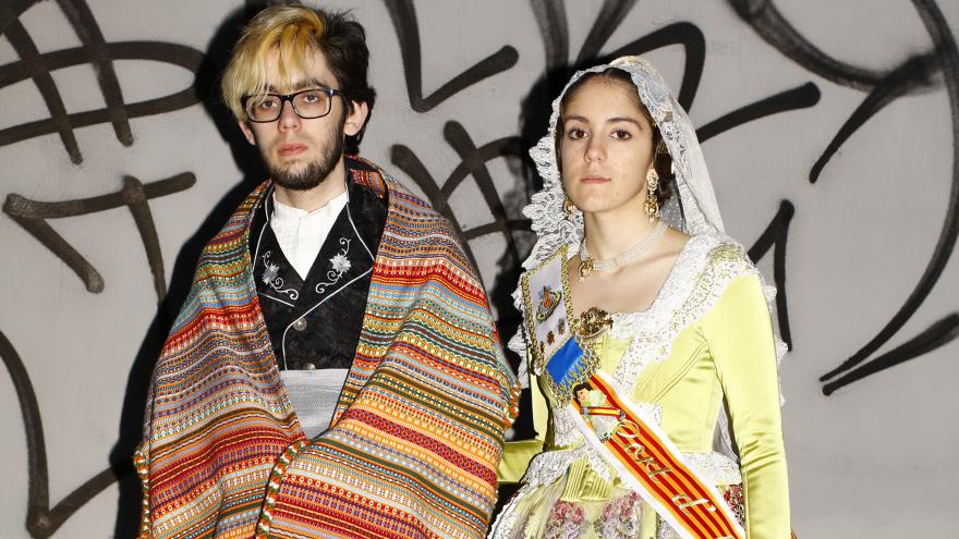 Dos jóvenes vestidos con traje regional de Valencia posando frente a un grafiti