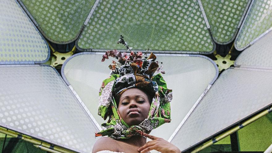 Mujer con un gran tocado frente a una arquitectura contemporánea de color verde