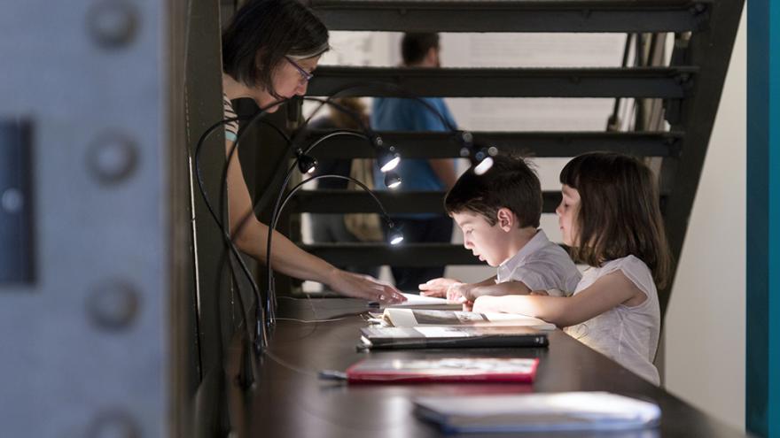 Dos niños mirando un libro en una vitrina de una sala de exposiciones